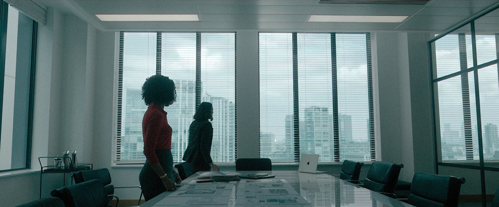 Backplates for film & TV by Will Pearson. The image is a still from The Woman in Cabin 10 © Netflix. It shows two women in an office setting with the London skyline visible through the office windows.